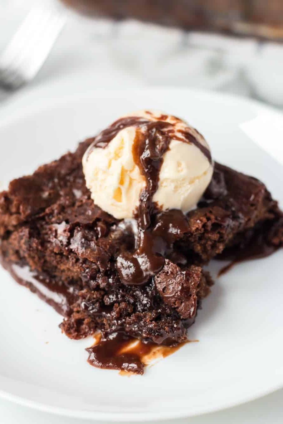 άσπρο πιάτο με σοκολατένιο γλυκό τύπου brownie, με μια μπάλα παγωτού βανίλιας από πάνω και σιρόπι σοκολάτας.