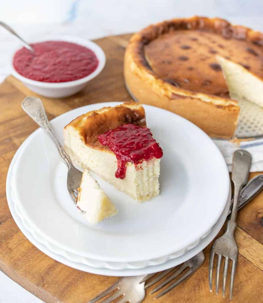 Τσιζκέικ της Μπεθ 5 Μια φέτα cheesecake με σάλτσα βατόμουρου σε πιάτο με το cheesecake στο παρασκήνιο.