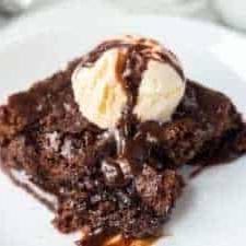 σοκολατένιο γλυκό τύπου brownie σε άσπρο πιάτο με μια μπάλα παγωτού βανίλιας από πάνω και σιρόπι σοκολάτας.