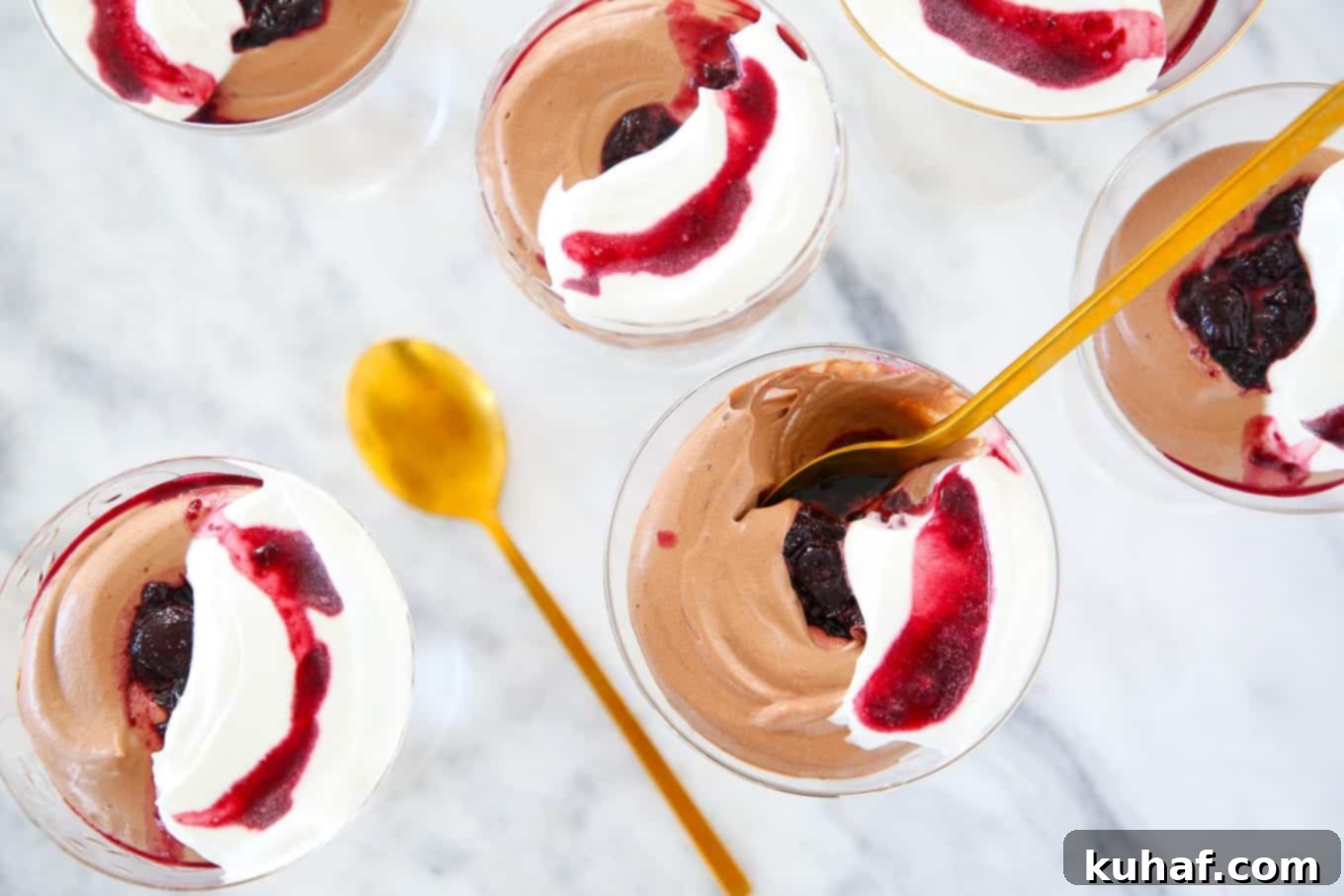 Two elegant coupes filled with smooth chocolate mousse, garnished with a cherry and a dollop of cream, resting on a white marble surface.