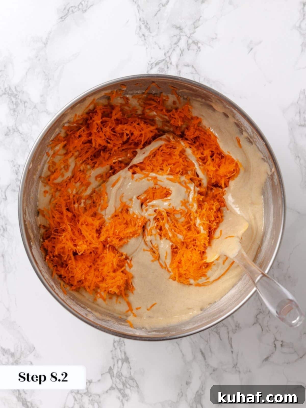 Grated carrots being added to the cake batter in a bowl.