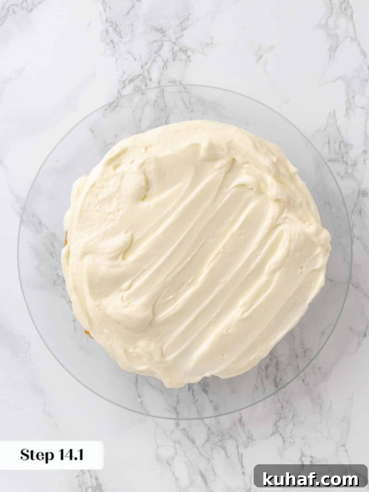 First cake layer covered in a smooth layer of cream cheese frosting.