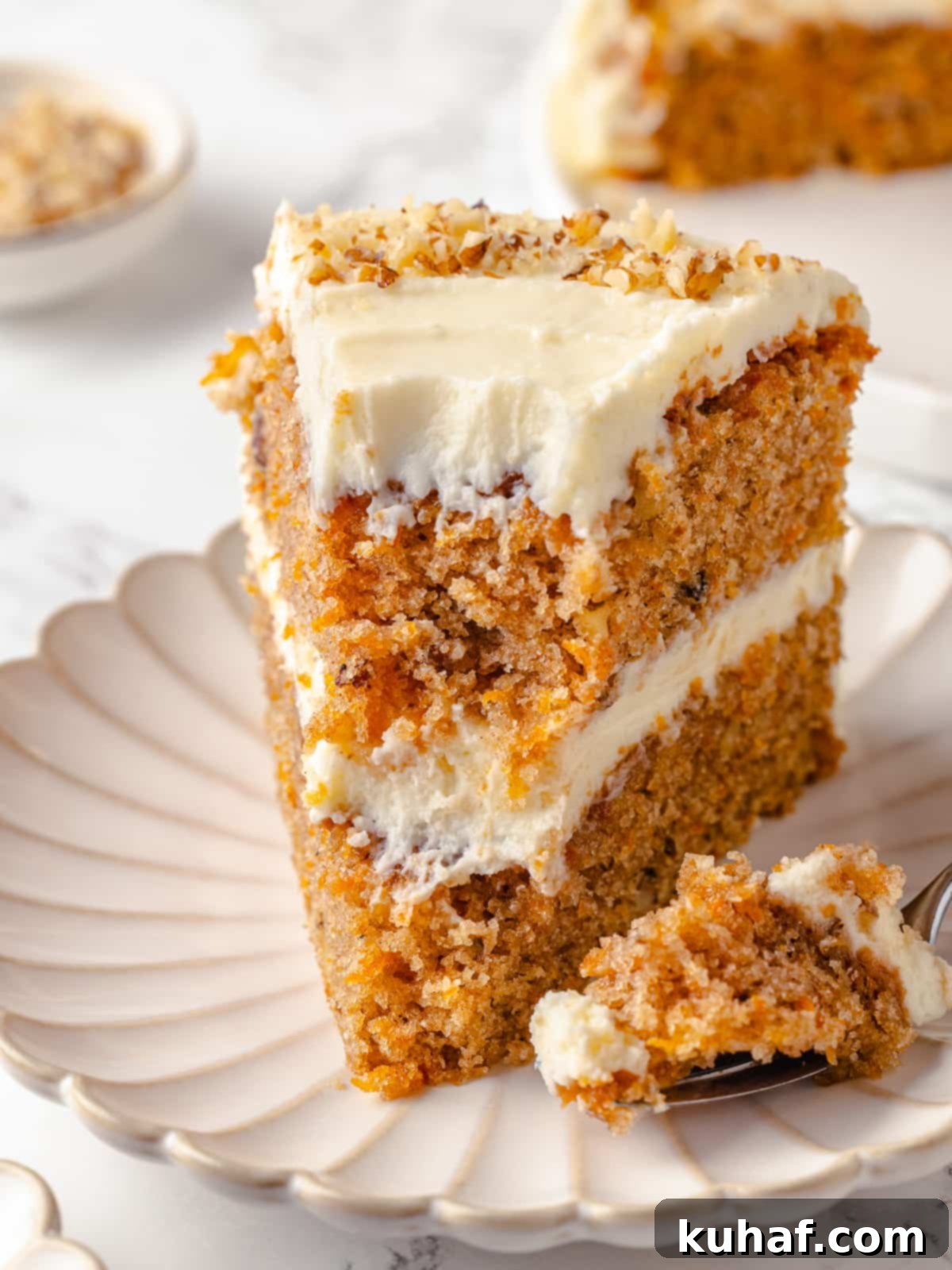 A forkful of moist carrot cake missing from a slice, showing its tempting texture.