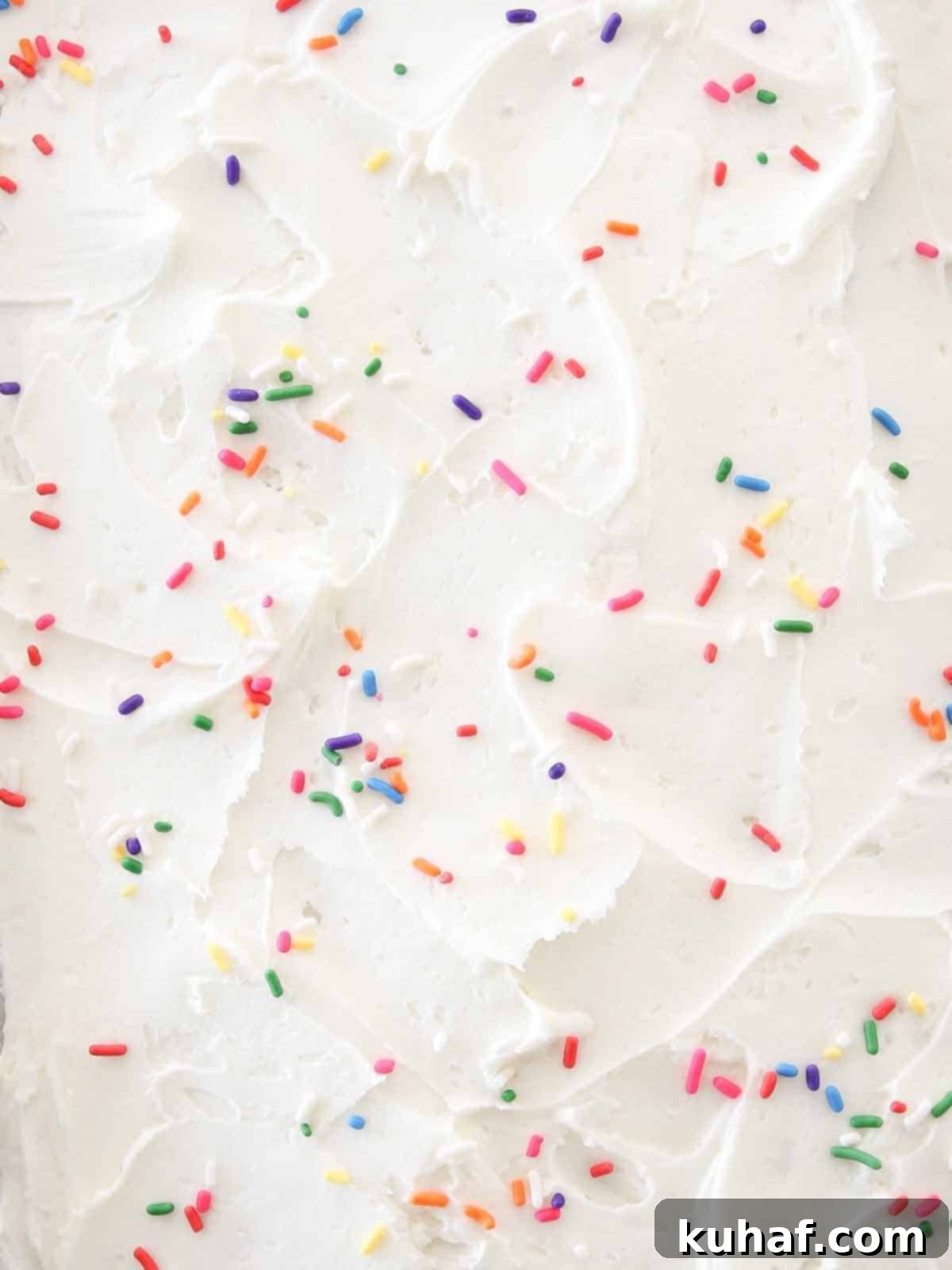 Swirled lemon buttercream frosting with colorful sprinkles decorating a Funfetti cake.