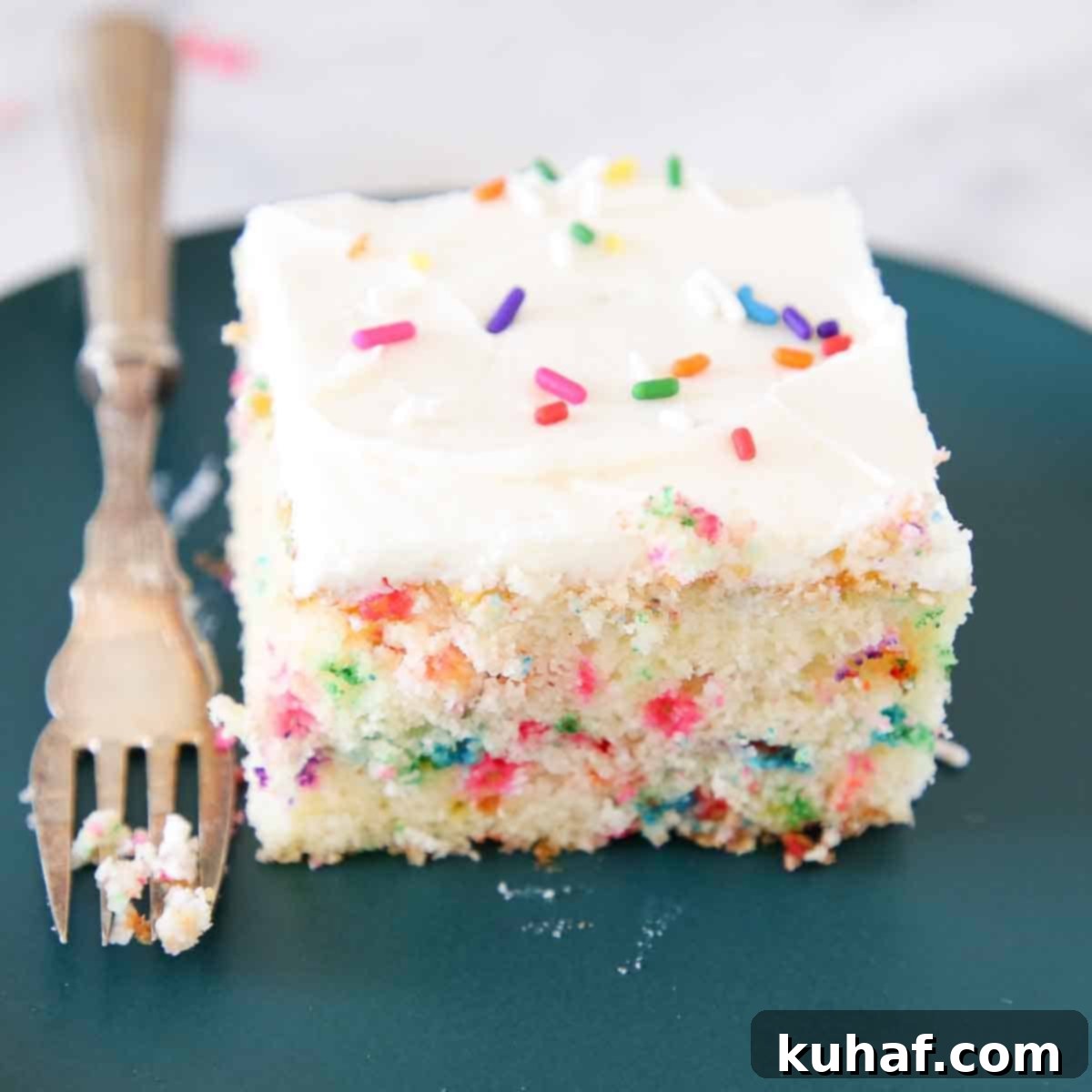 A beautiful slice of Funfetti cake on a green plate with a vintage fork, showing soft crumb and sprinkles.