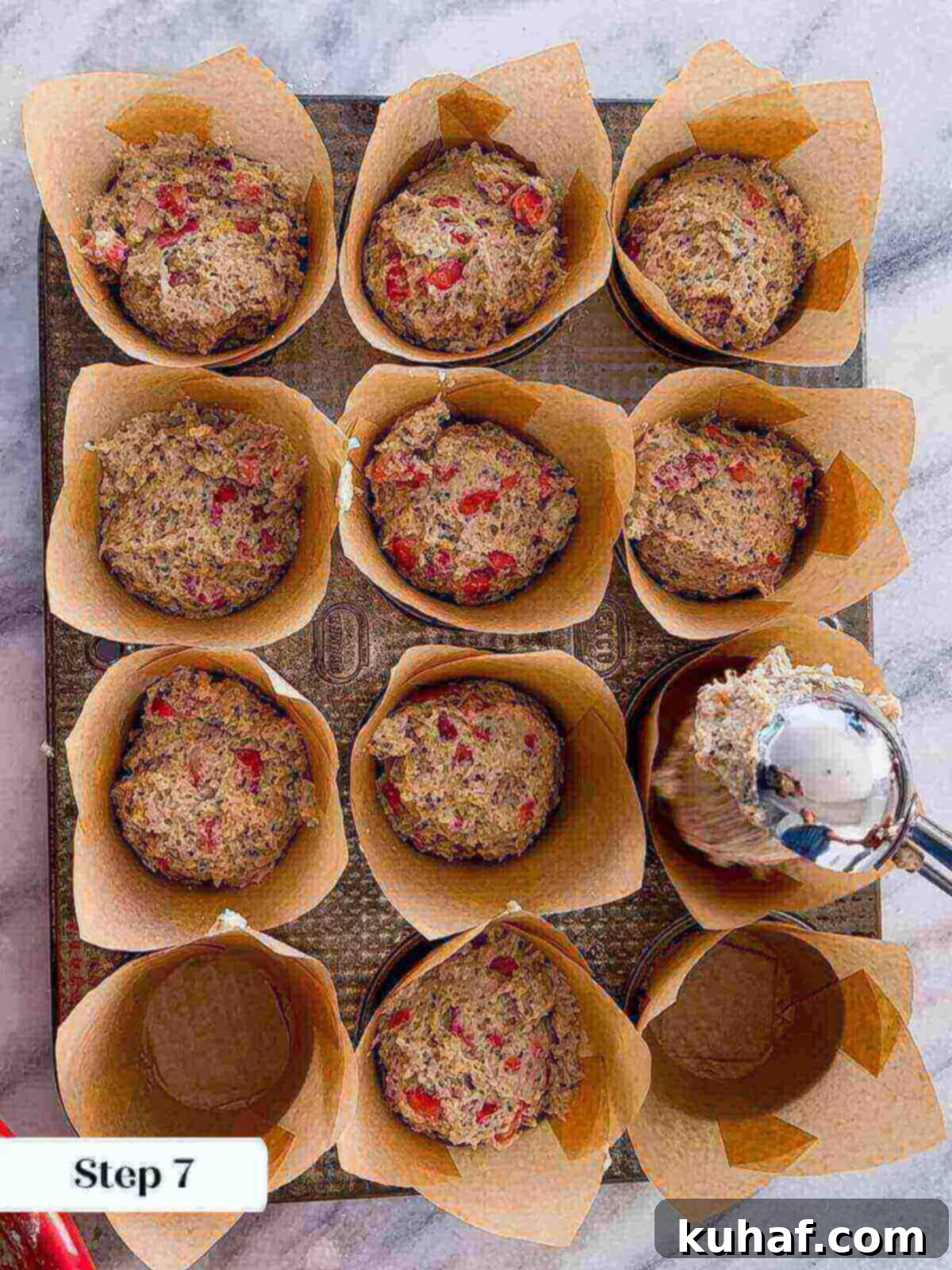 Delicious Strawberry Muffins 10 Muffin batter being portioned evenly into individual paper-lined muffin cups using a scoop.