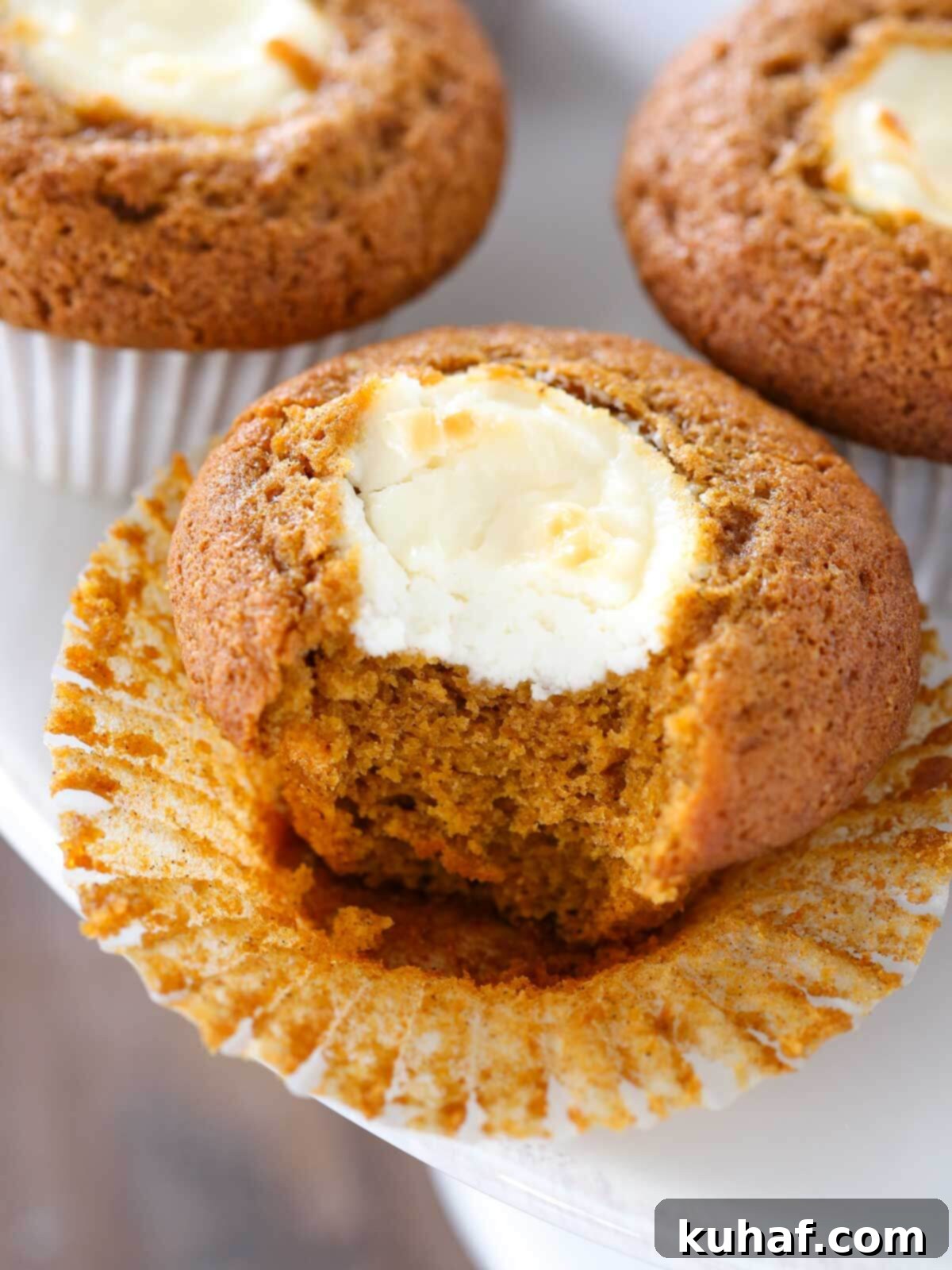 Soft and moist pumpkin cream cheese muffin, unwrapped, showcasing its creamy filling on a rustic cake stand, ready to be enjoyed.