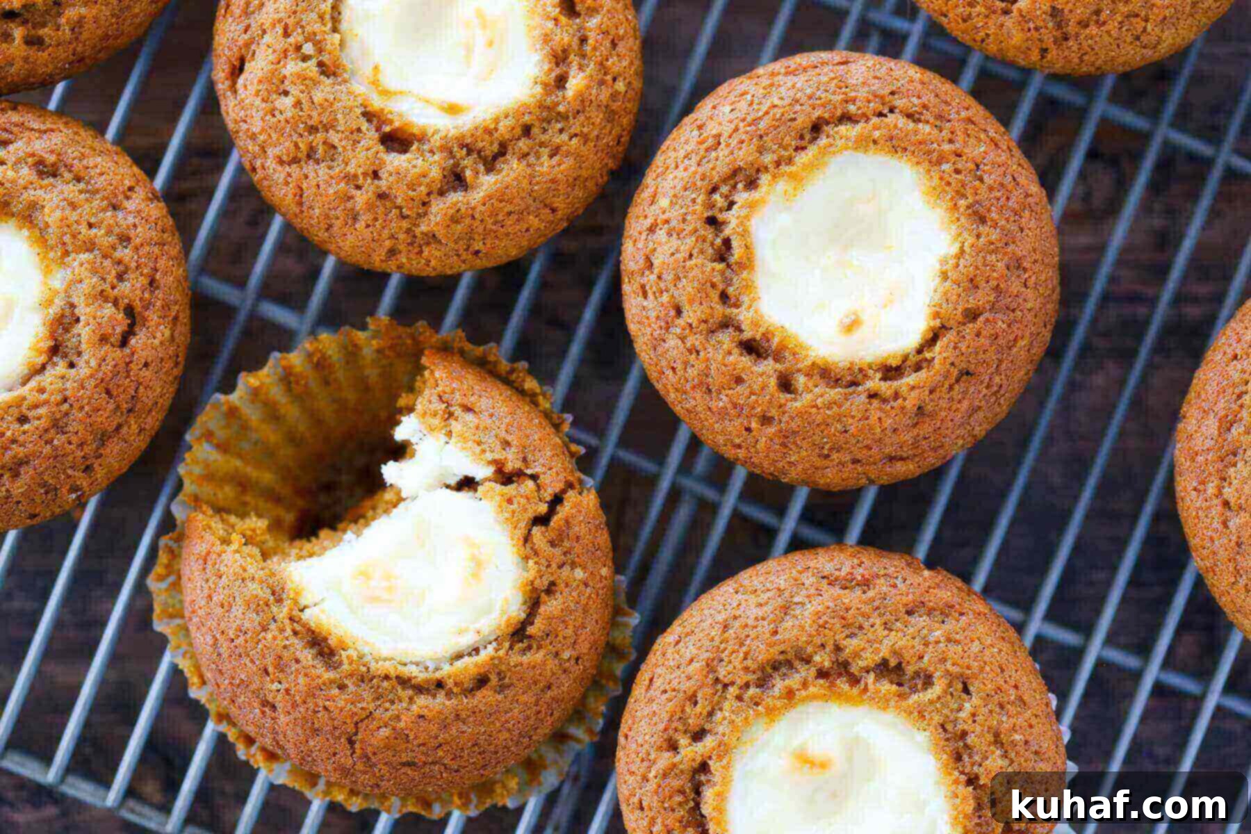 Freshly baked pumpkin cream cheese muffins cooling on a wire rack, showing their golden tops and visible creamy centers.