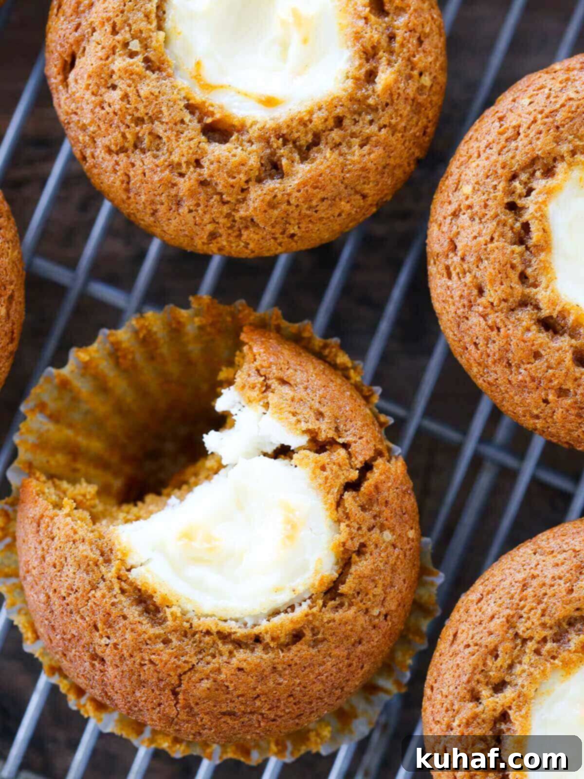 A delicious pumpkin muffin unwrapped, with a bite taken out, revealing the creamy vanilla cream cheese filling inside.