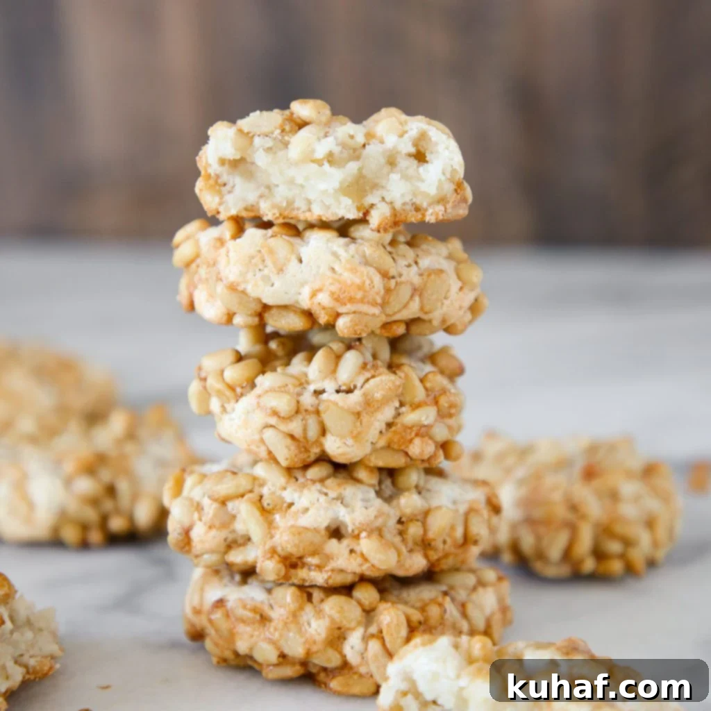 A stack of 5 baked pignoli cookies, showcasing their golden pine nut exterior.