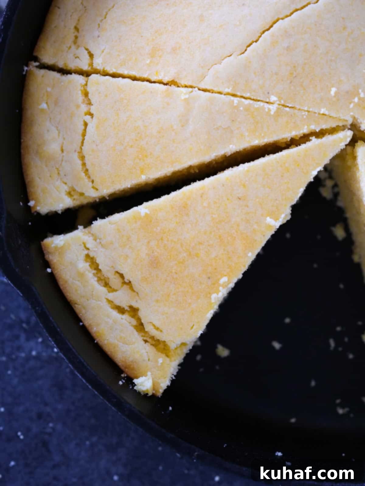 Sliced Southern cornbread in a black cast iron skillet with a golden brown top, emphasizing its moist texture.