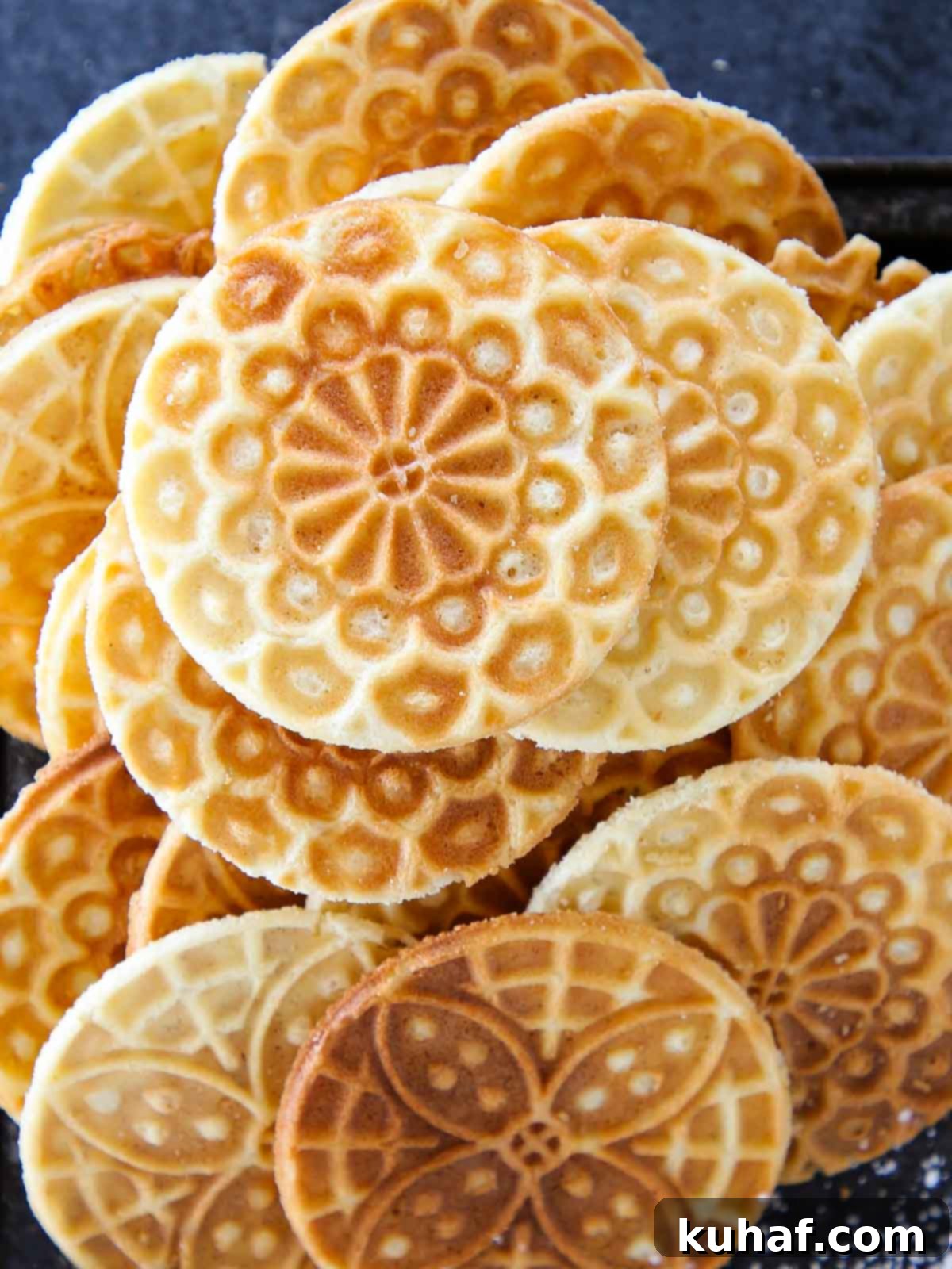Pizzelle cookies piled on a black tray, dusted lightly with powdered sugar.