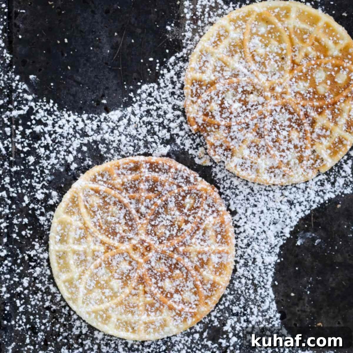 Close-up of golden brown pizzelle cookies dusted with powdered sugar.