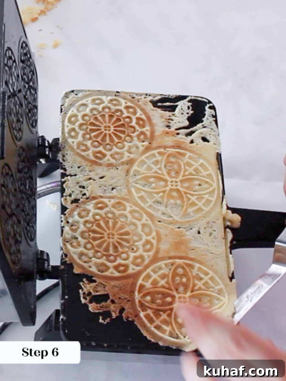 Golden brown pizzelles in the iron, being removed with a spatula.