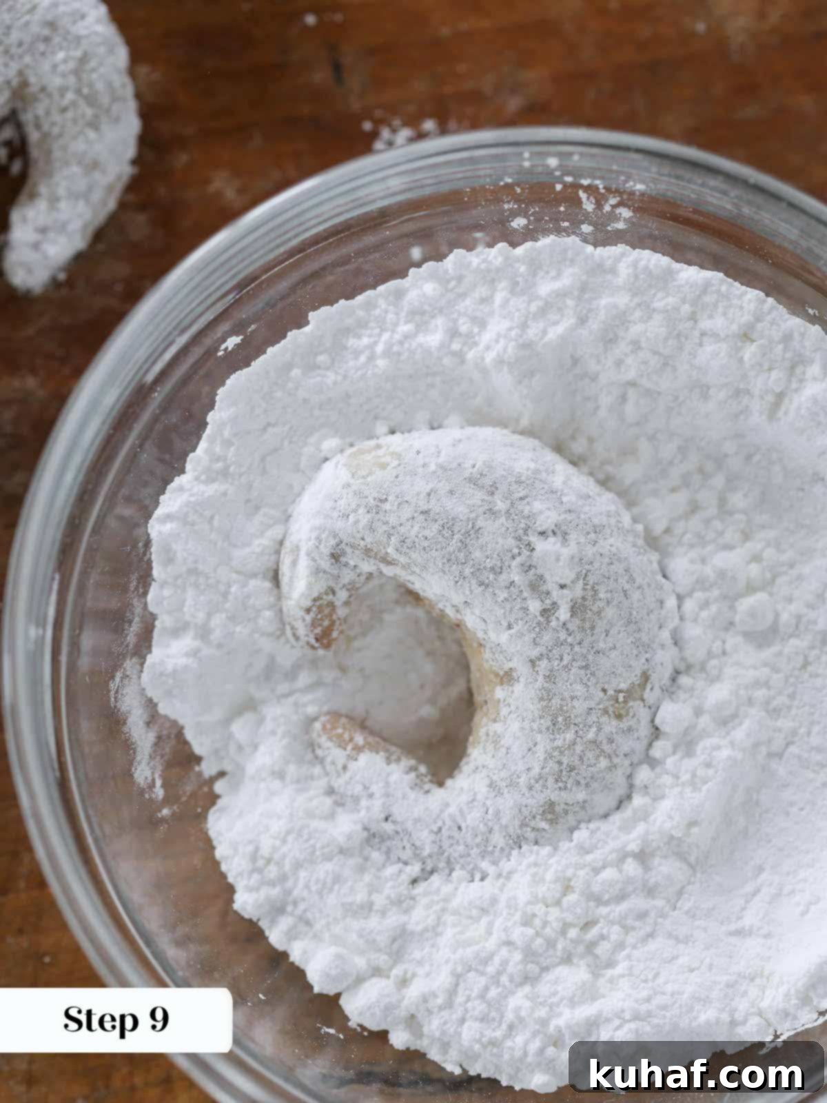 A crescent cookie being tossed in a bowl of vanilla bean powdered sugar.