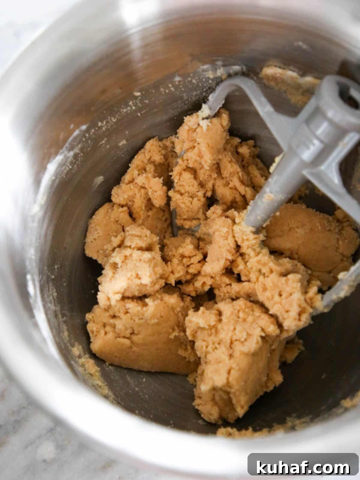Cookie dough in a silver stand mixer bowl, being creamed.