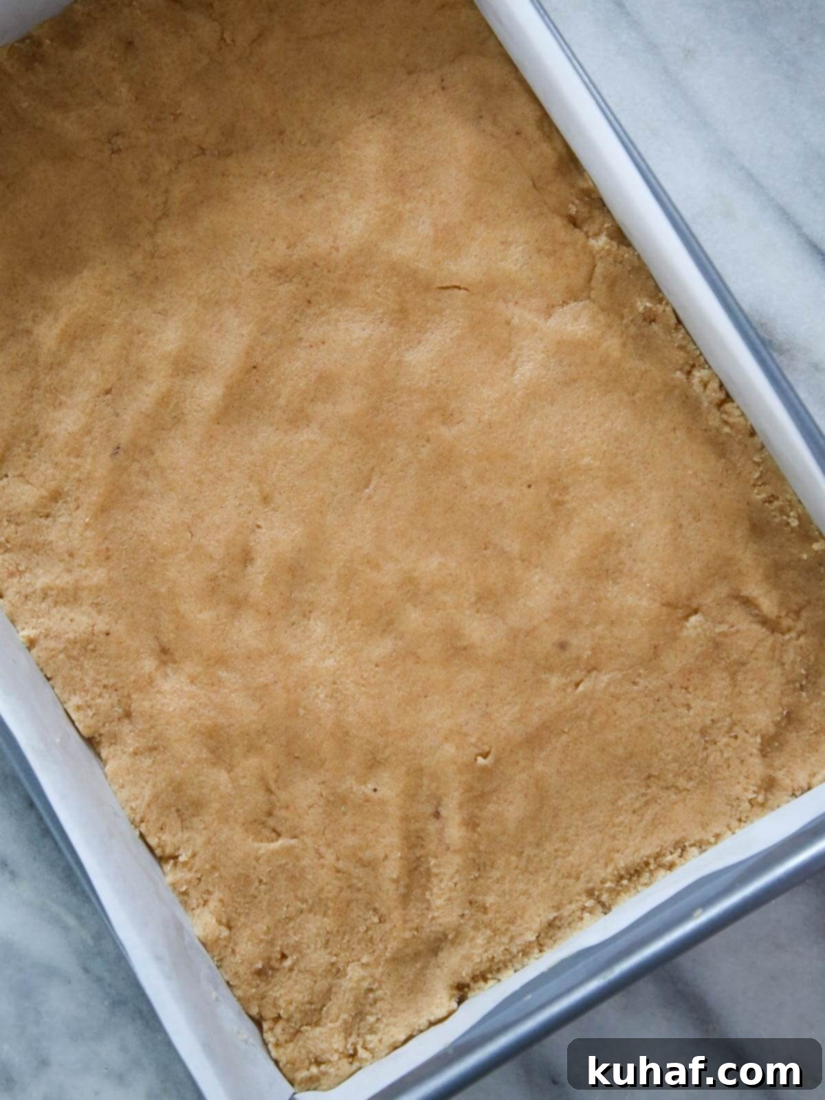 Cookie dough pressed evenly into a silver baking pan.