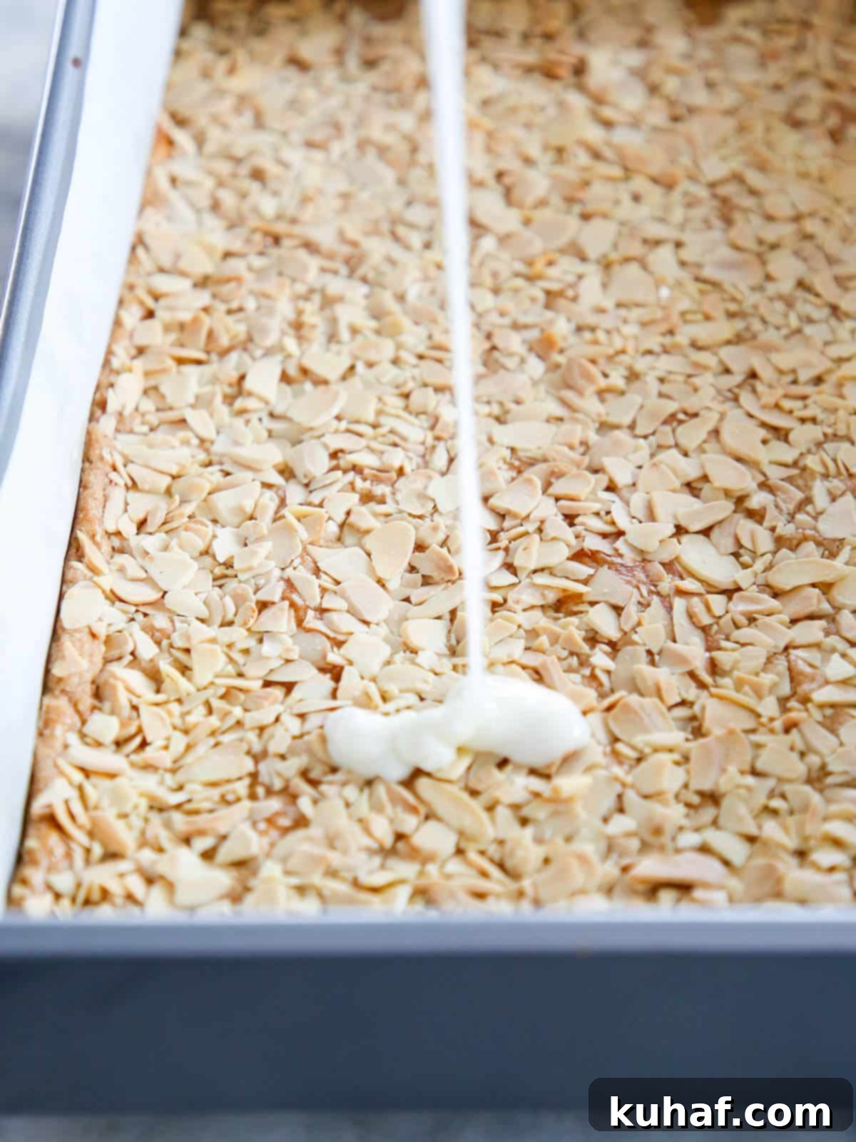 White lemon glaze pouring down onto the warm almond topping of baked bars.