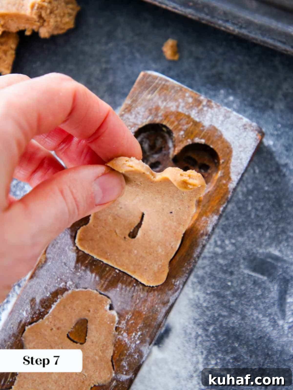 A crisp speculoos cookie being carefully peeled out of a wooden mold, revealing its detailed pattern.