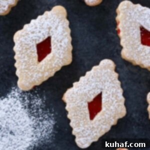 Raspberry Linzer Cookies on dark surface with extra powdered sugar.
