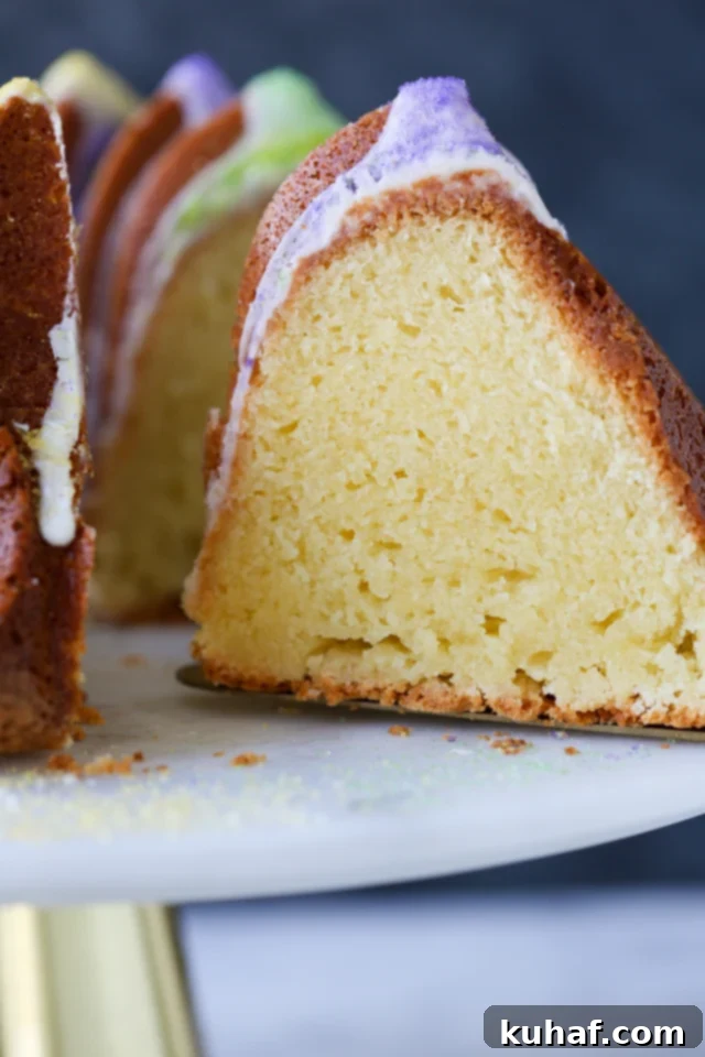 Close-up of a slice of Mardi Gras Bundt Cake removed from the whole cake, showing its moist interior, rich glaze, and festive sprinkles.