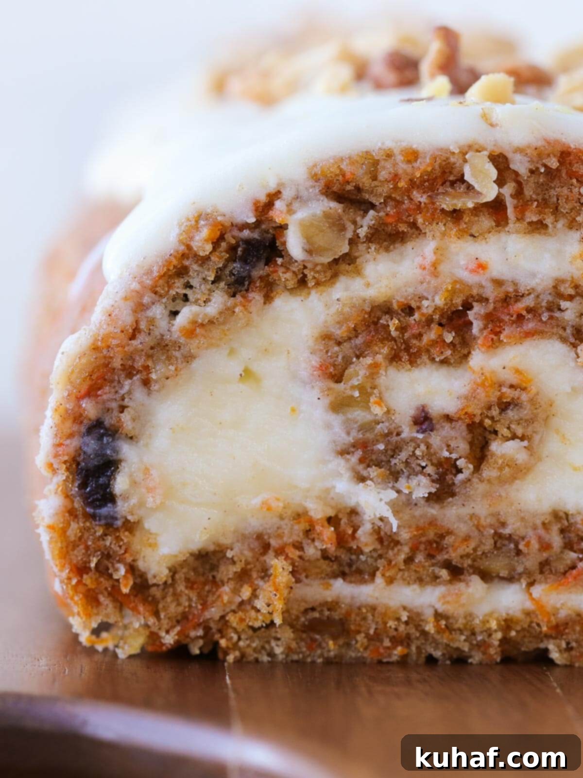 Deliciously moist carrot cake roll sliced into serving portions, topped with a generous layer of cream cheese frosting and a light dusting of powdered sugar, showcasing the perfect spiral layers.