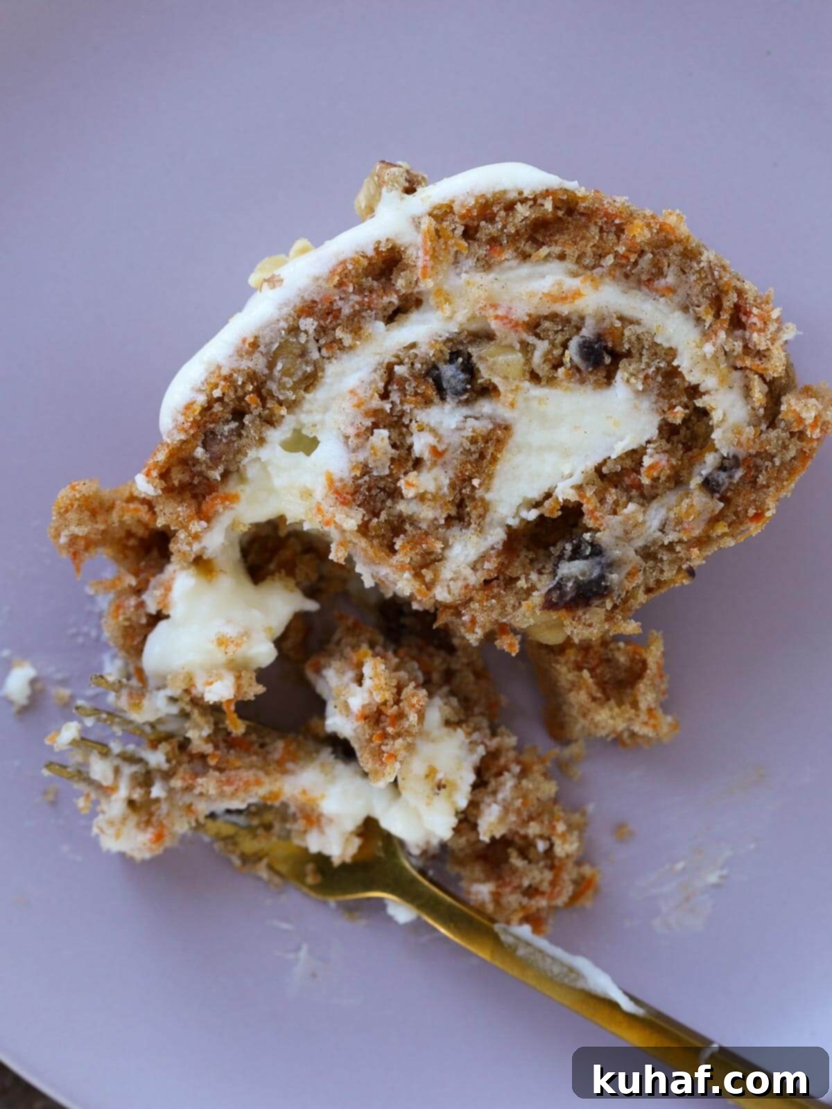 A carrot cake roll in progress, showing the cake being rolled tightly with cream cheese frosting spread inside. The spiral is clearly visible.
