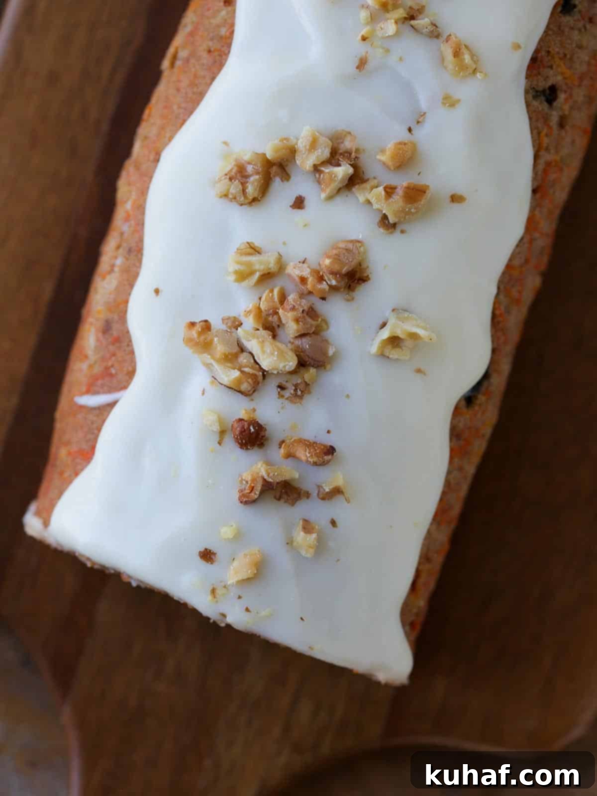 A perfectly sliced carrot cake roll on a wooden serving board, beautifully dusted with powdered sugar, showcasing the intricate spiral of moist cake and creamy white frosting, with a few extra walnuts and cranberries for garnish.