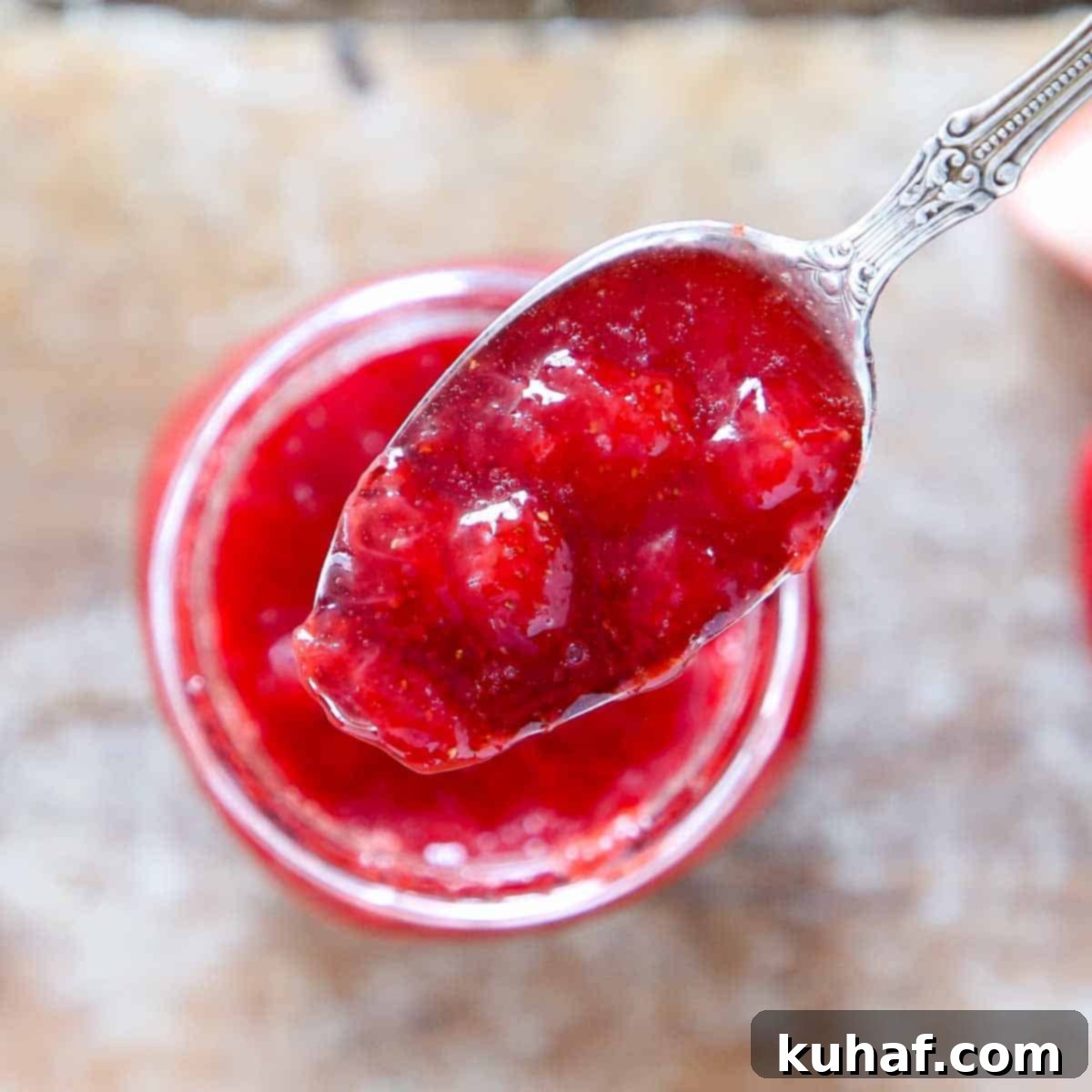 Homemade strawberry jam presented on a large spoon, held invitingly over a rustic jar filled with more jam.