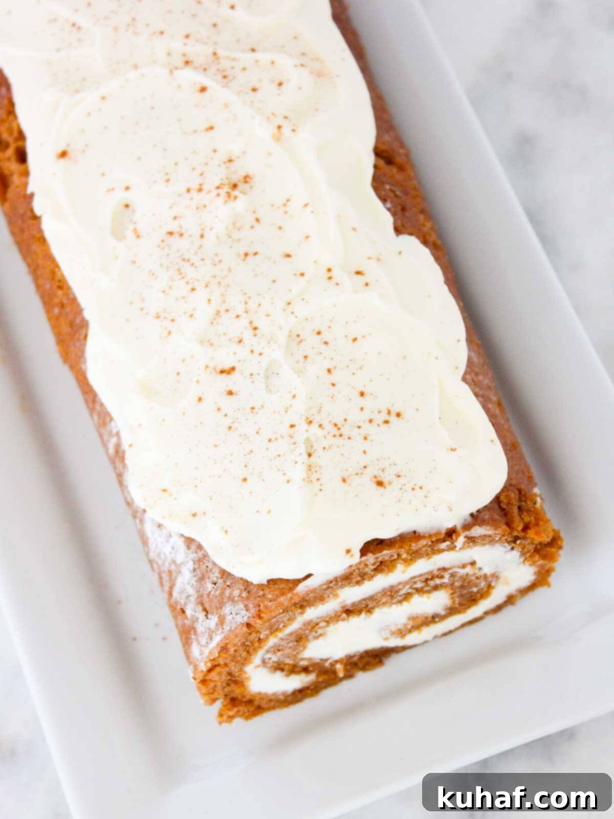 Irresistible Autumn Pumpkin Roll 3 unsliced pumpkin roll with cream cheese frosting on top.