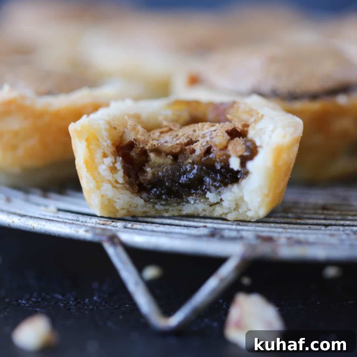 Pecan tassie on a dark background with flaky layered crust.