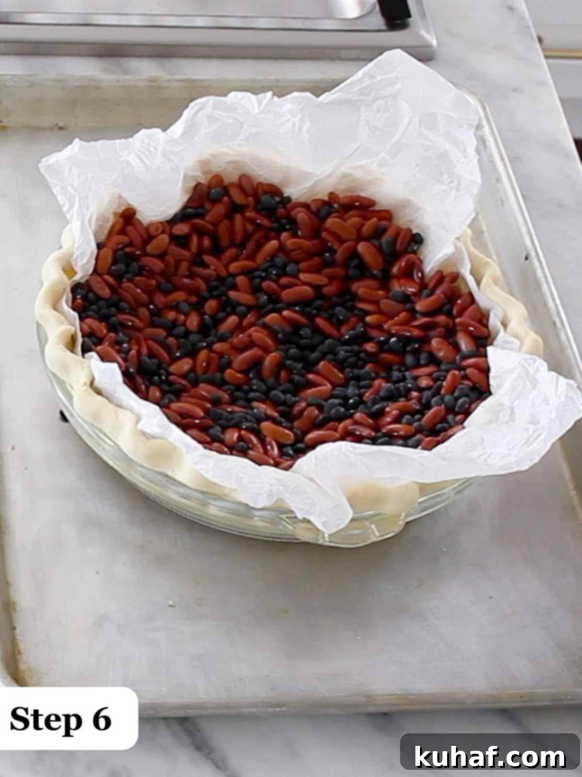 Step 6: A pie crust undergoing blind baking, filled with dried beans acting as pie weights.