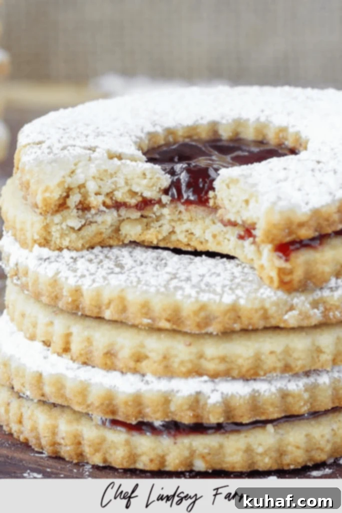 A stack of raspberry linzer cookies with the top one bitten.