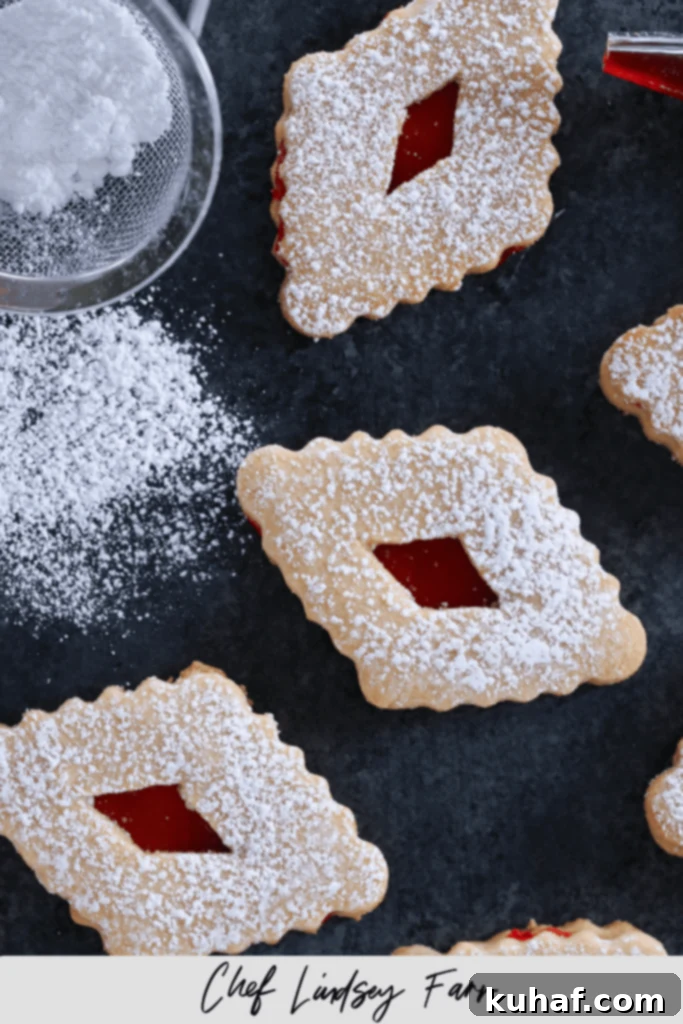 Raspberry linzer cookies laid out on a dark background with powdered sugar sifter nearby.