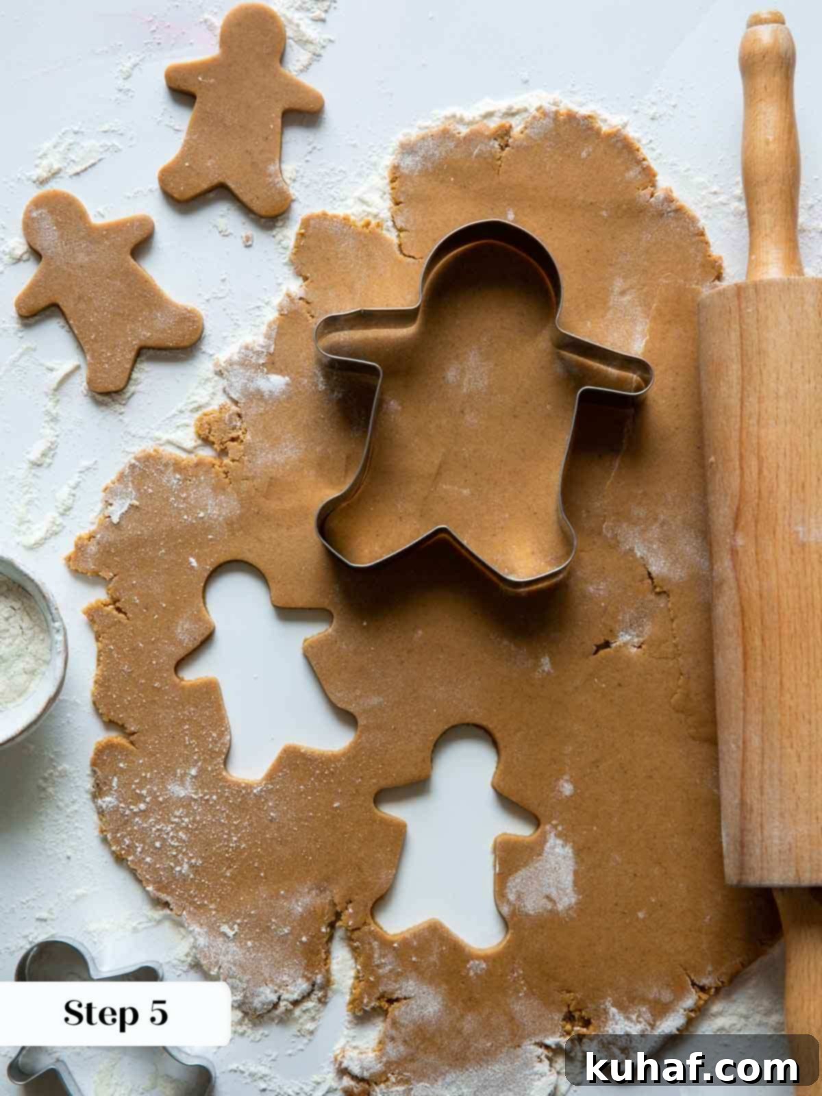 Gingerbread dough being rolled and cut with holiday cookie cutters.