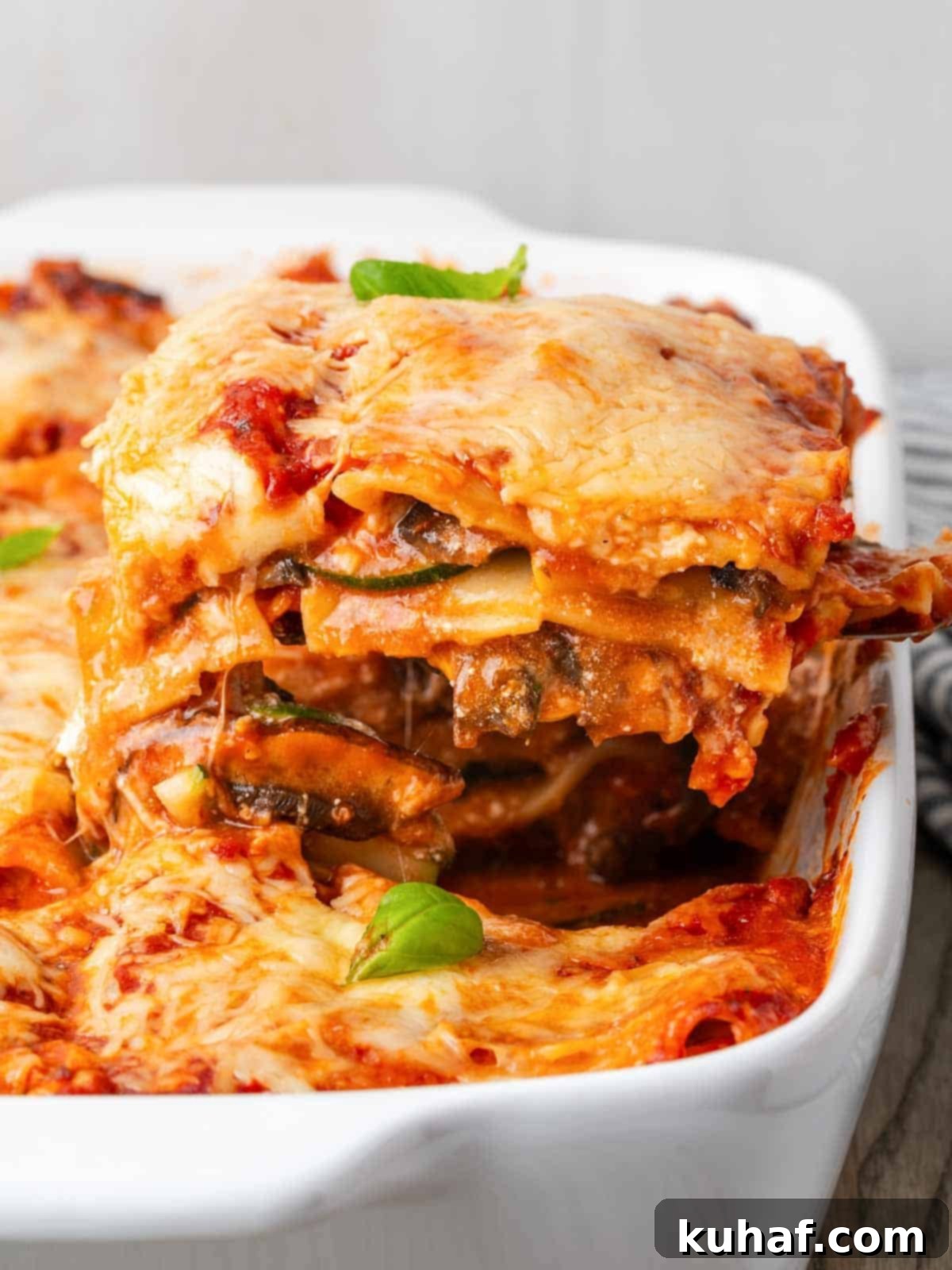A perfectly sliced portion of vegetable lasagna resting on a white serving dish, showcasing its layers of pasta, cheese, and vegetables.