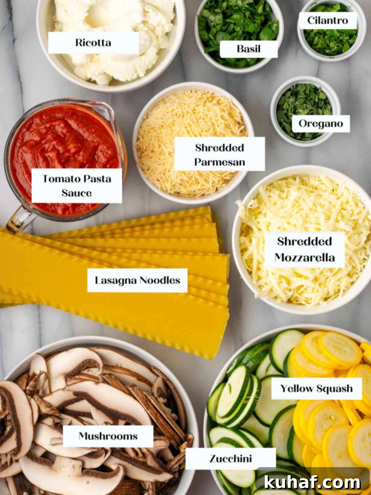 A collection of fresh ingredients for vegetable lasagna laid out on a white marble surface, including zucchini, squash, mushrooms, herbs, cheeses, and pasta.