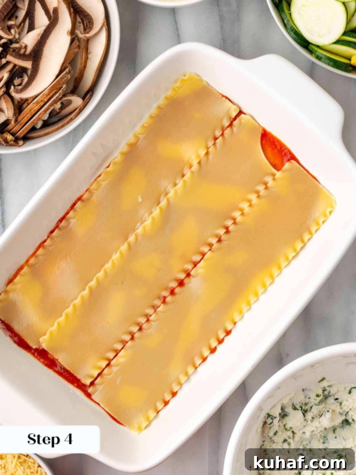 A thin layer of tomato sauce at the bottom of a baking dish, with the first layer of lasagna noodles being placed over it.