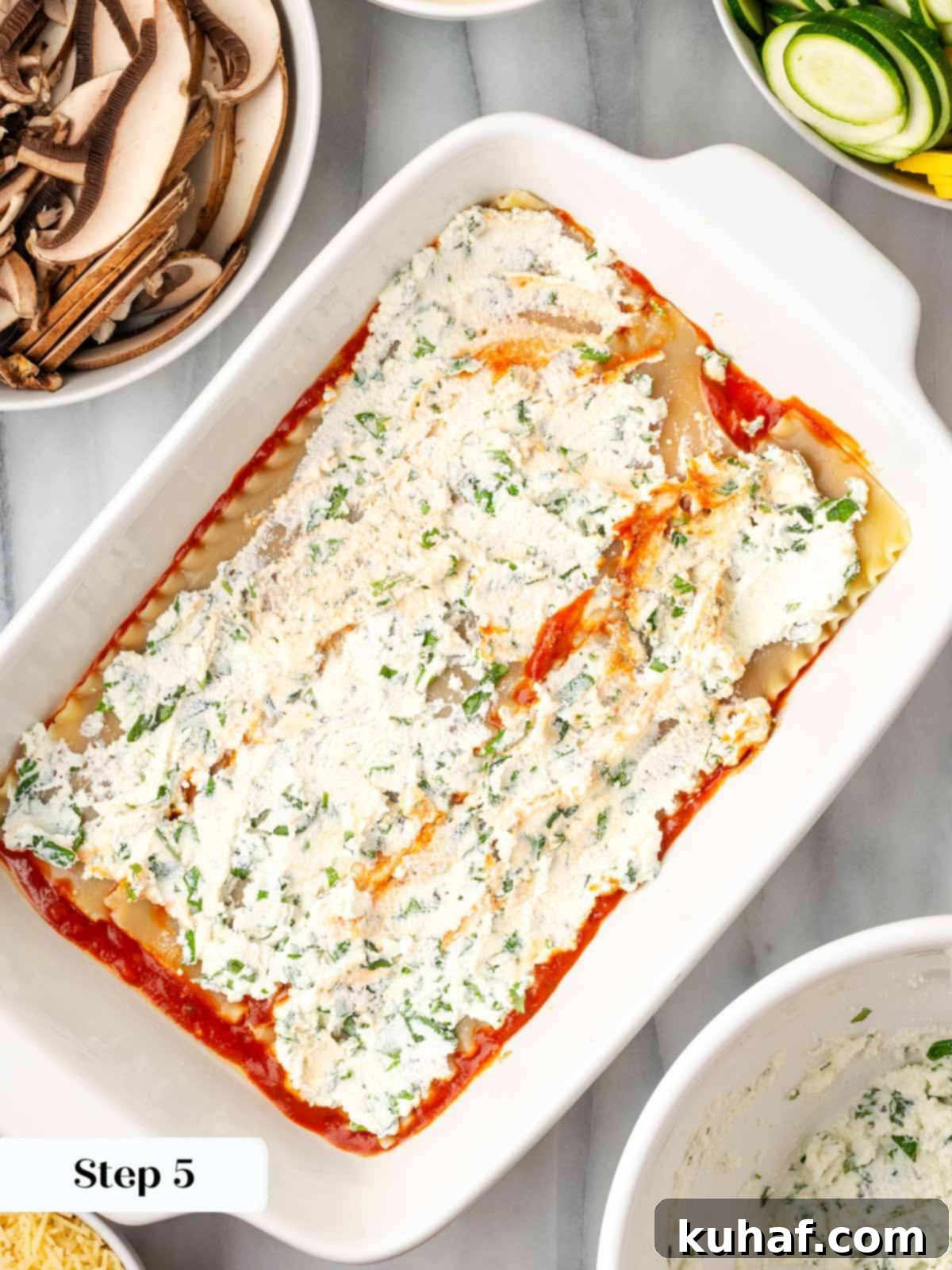 A layer of ricotta cheese mixture being spread evenly over the lasagna noodles in the baking dish.