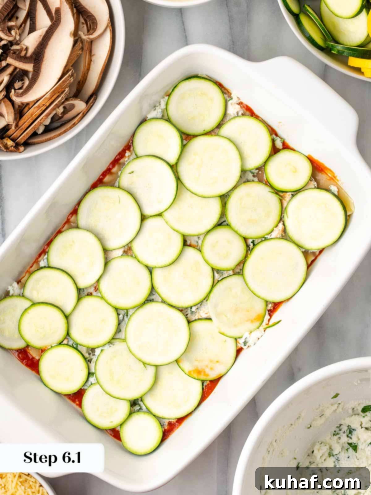 Thinly sliced zucchini being arranged in an even layer over the ricotta in the lasagna dish.