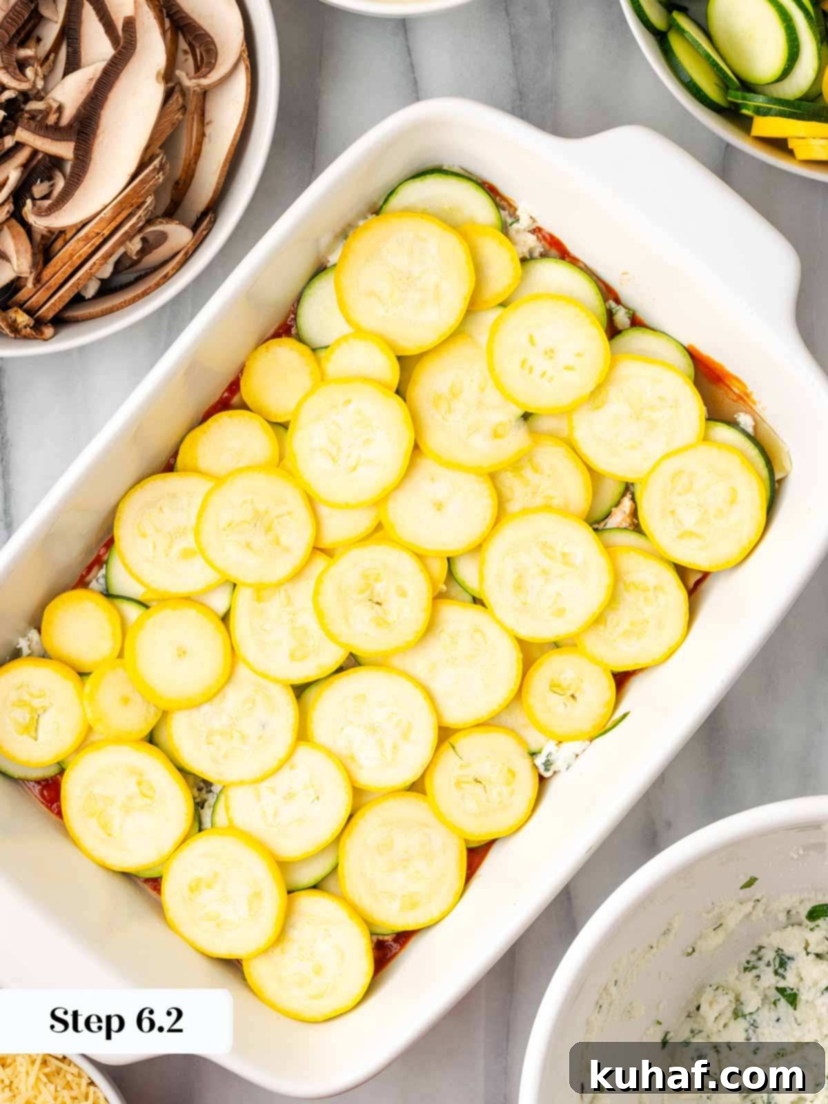 Thinly sliced yellow squash being placed over the zucchini layer in the lasagna dish.