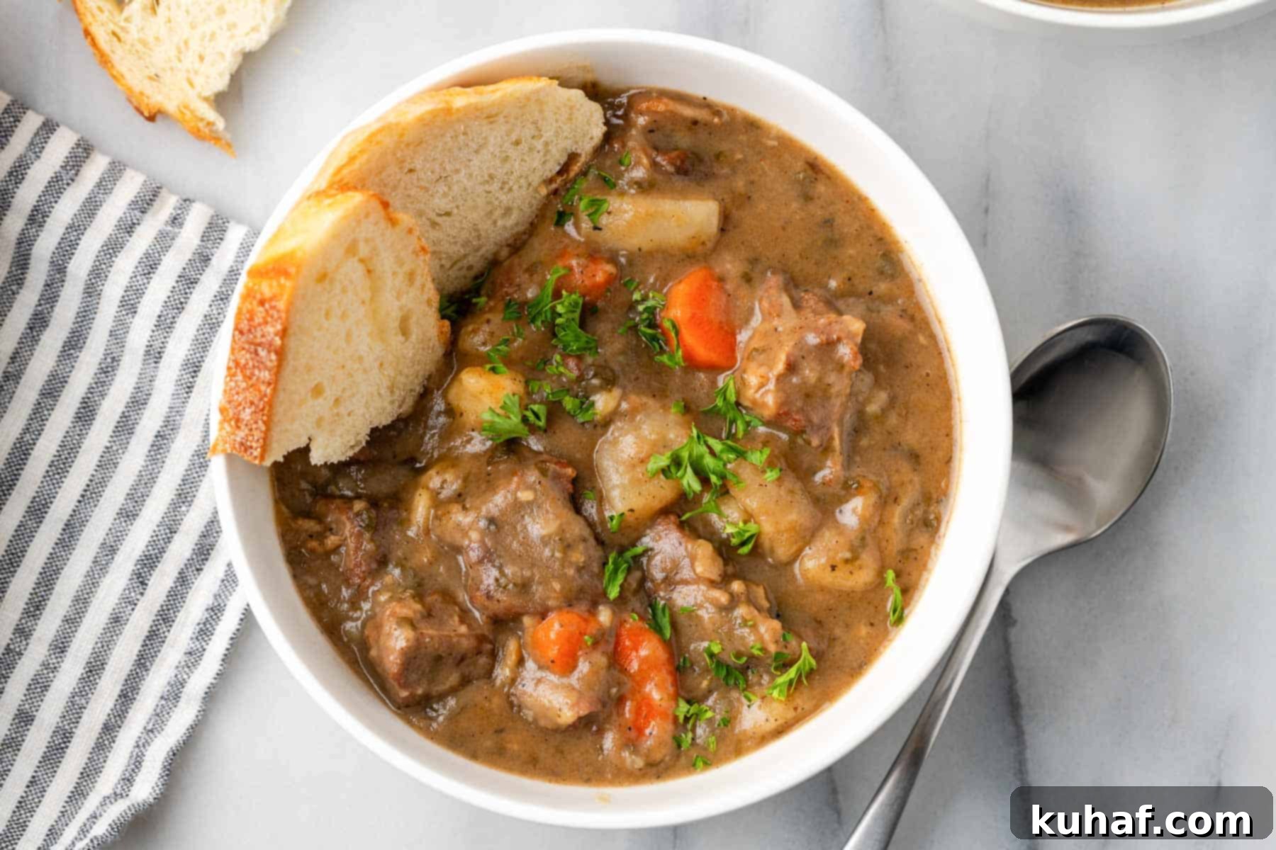 Hearty beef stew served in a white bowl with a side of soda bread, garnished with fresh herbs.