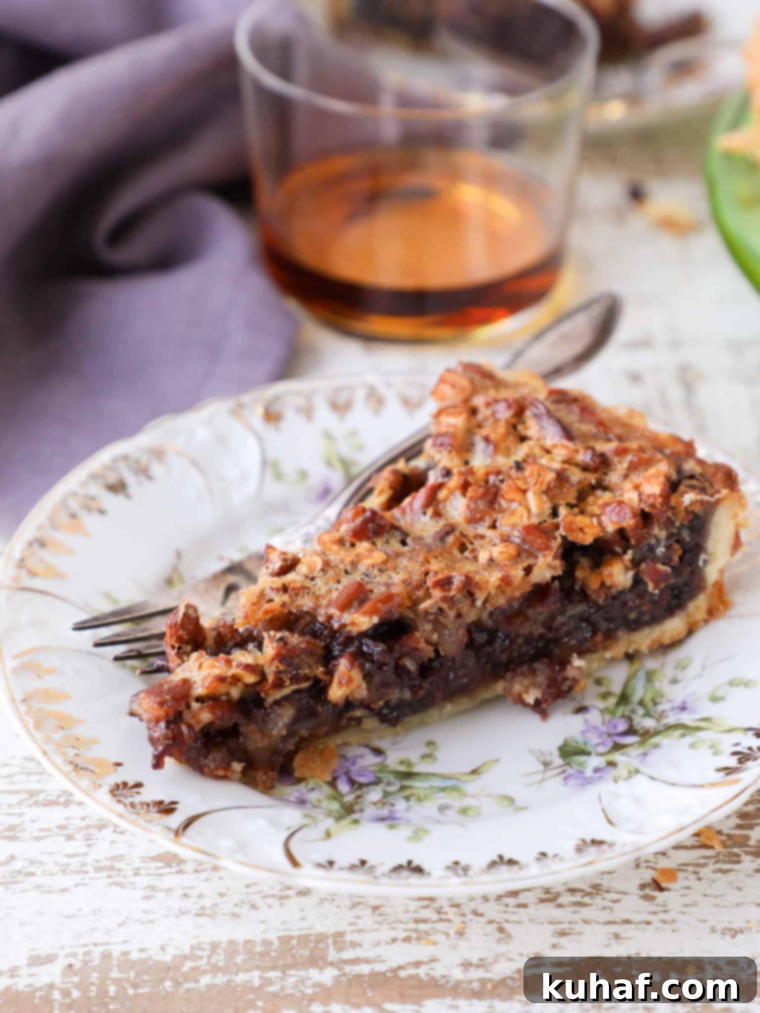 A perfectly baked slice of Bourbon Chocolate Pecan Tart on a plate with a purple napkin, showing the golden crust and rich filling.