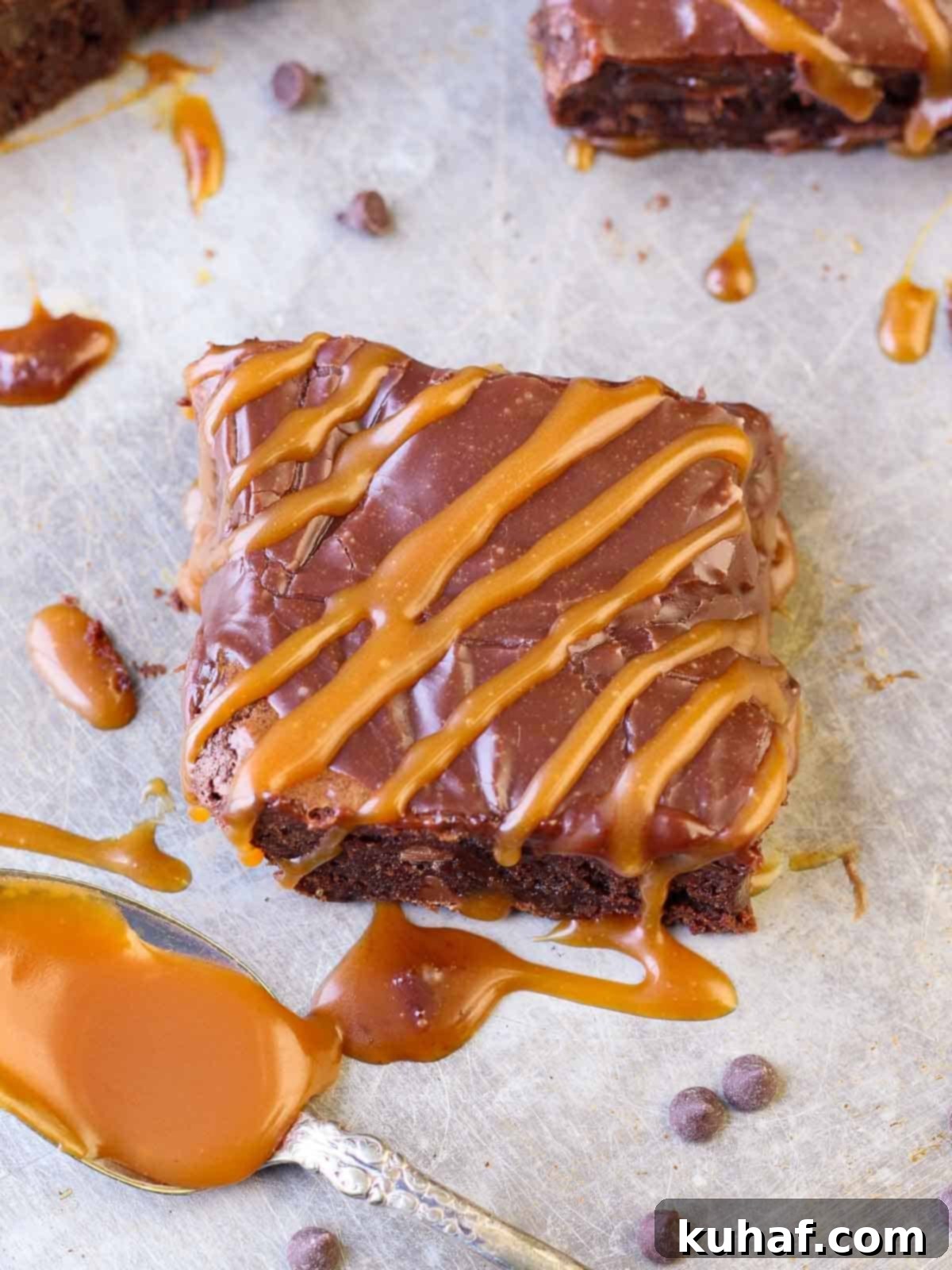 A close-up of a single serving of caramel brownie, cut from the pan, showing its thick, fudgy texture, the luscious ganache topping, and the delicate caramel swirl within.