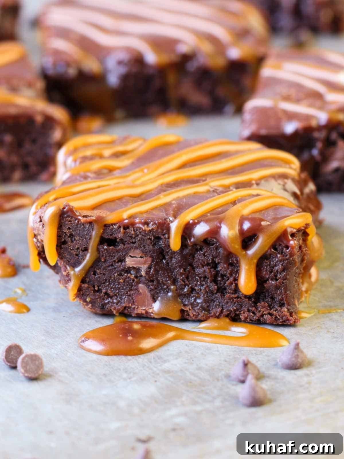 A slice of a fudgy caramel brownie with visible layers of rich milk chocolate brownie, gooey salted caramel swirls, and a smooth Baileys ganache topping, ready to be enjoyed.