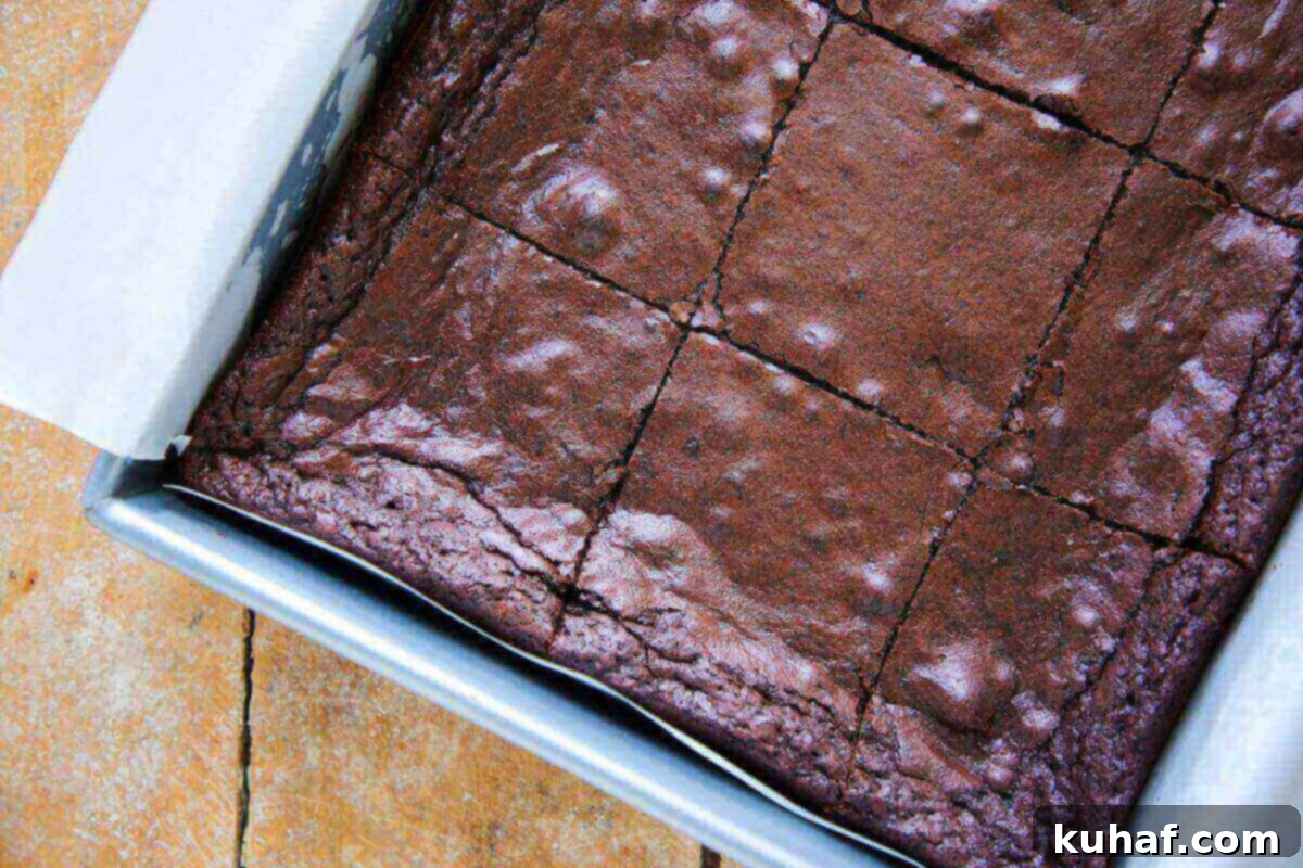 A pan of freshly sliced one-bowl brownies cooling on a wooden table, showcasing their perfect texture.