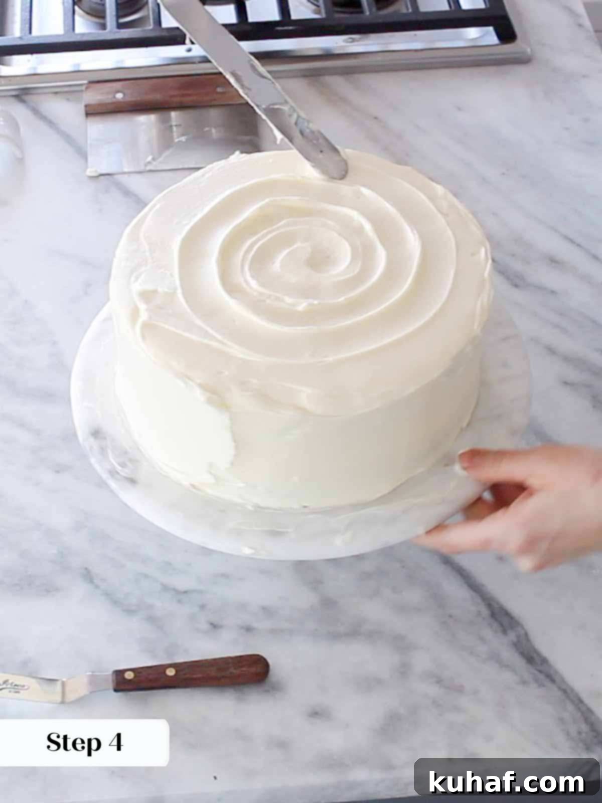 A close-up of a cake decorator swirling the top layer of cream cheese buttercream on a hummingbird cake, creating an elegant texture.