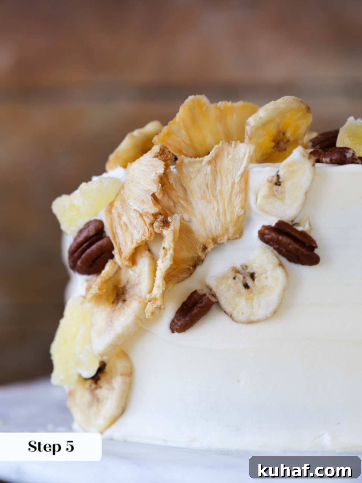 A fully decorated hummingbird cake, showcasing an intricate mosaic pattern of dried fruits and pecans on its creamy frosting.