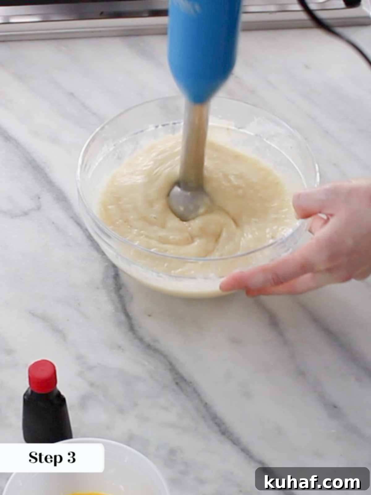 Close-up of an immersion blender smoothly combining pineapple and banana in a bowl, creating a uniform puree.