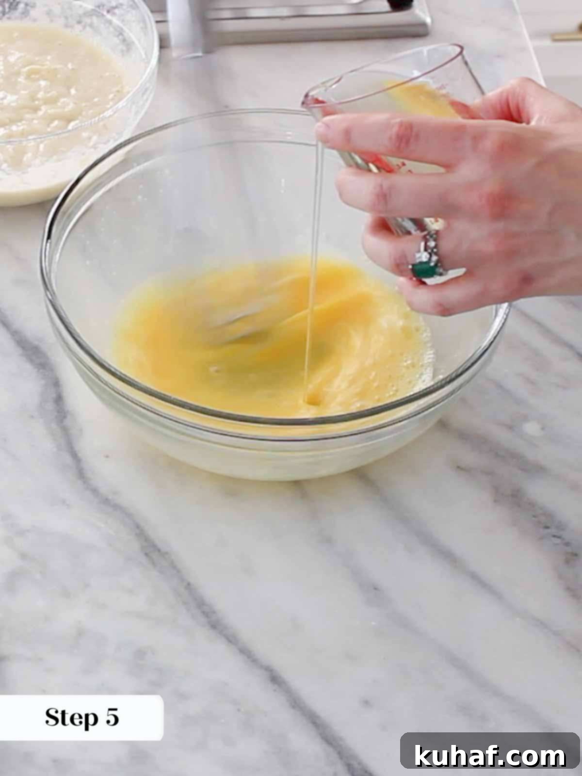 A stand mixer whisk attachment expertly emulsifying oil into beaten eggs, creating a smooth, glossy mixture.